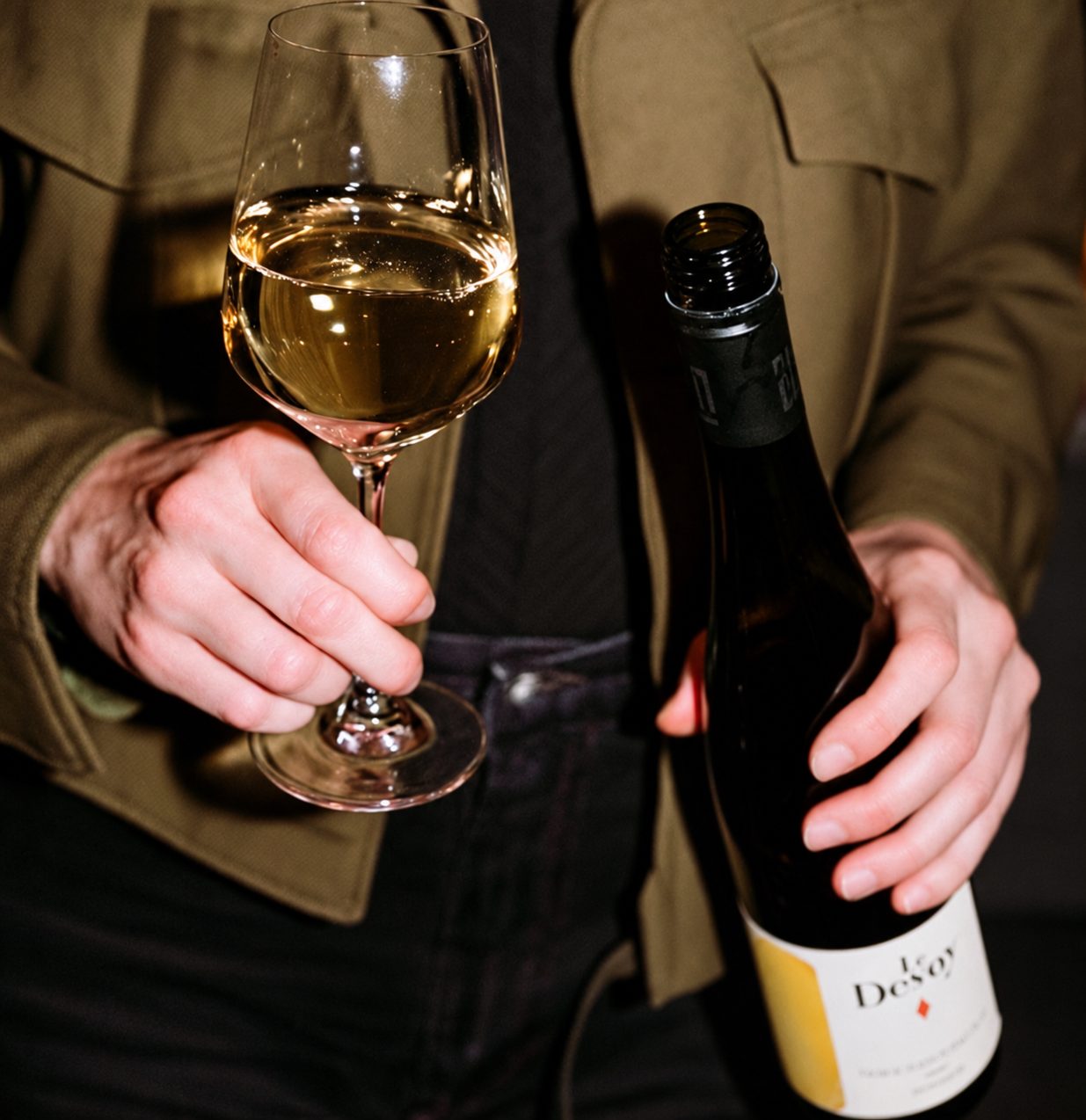 Hands holding a glass of white wine and a bottle